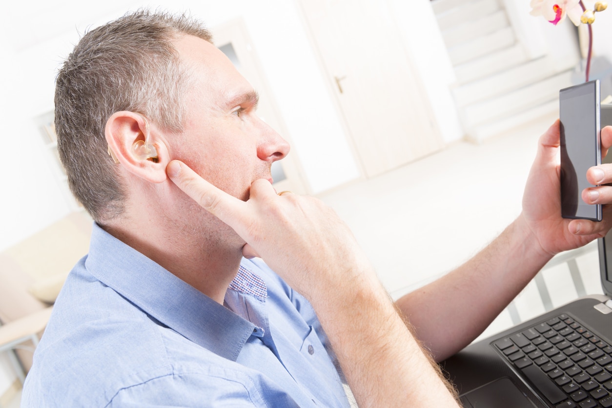 Man with hearing loss looks at phone at work