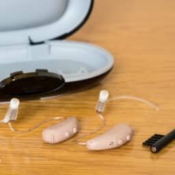 Hearing aids on a table with a cleaning brush and dryer box.