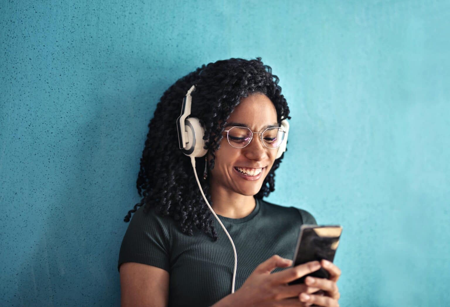 A happy person listens to an audiobook on their phone through headphones.