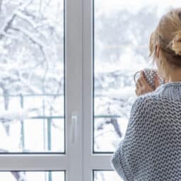 Woman drinking tea and looking out the window at her snowy Maine backyard