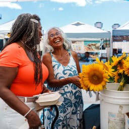 Woman and her mother happily browse an outdoor flower market on a beautiful day in Maine.