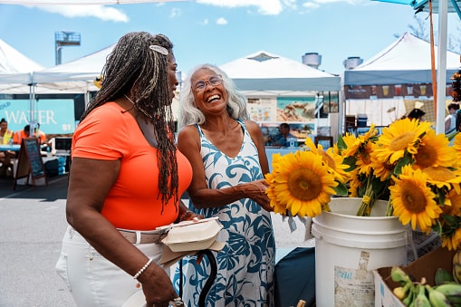 Woman and her mother happily browse an outdoor flower market on a beautiful day in Maine.