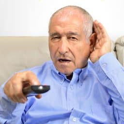 Senior man cupping his hand behind his ear to hear better to the television